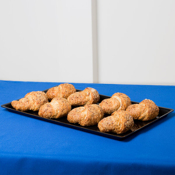 A Cal-Mil black bakery tray with croissants on a table with a blue tablecloth.