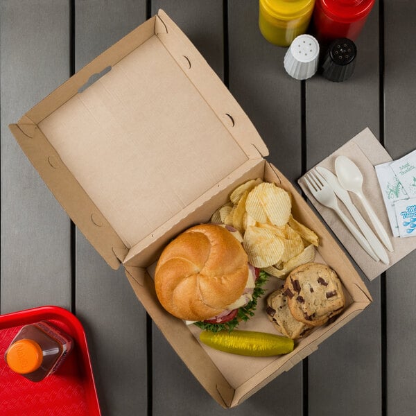 A Bagcraft Eco-Flute paper take-out box on a table with a sandwich, chips and a drink.
