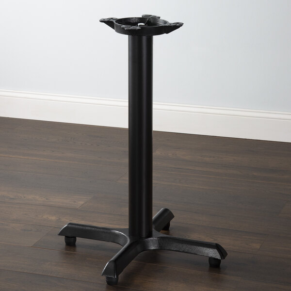 A Lancaster Table & Seating black standard height column table base on a wood floor.