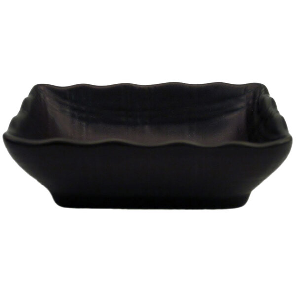 A black stoneware sauce dish with scalloped edges.