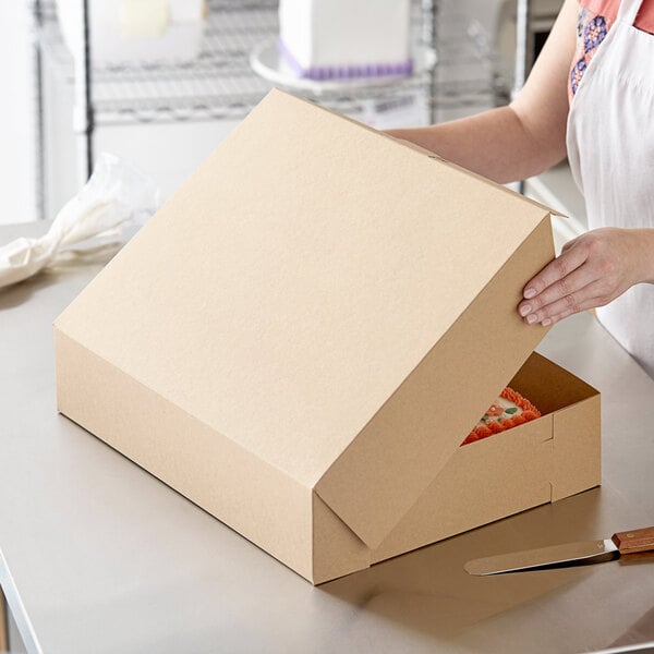 A woman opening a Baker's Mark Kraft bakery box with a cake inside.