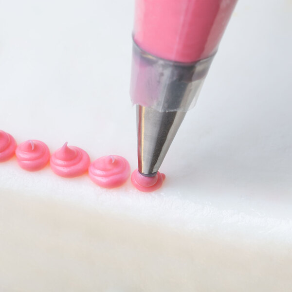 A person using an Ateco oval tip on a pink pastry bag to pipe pink frosting.