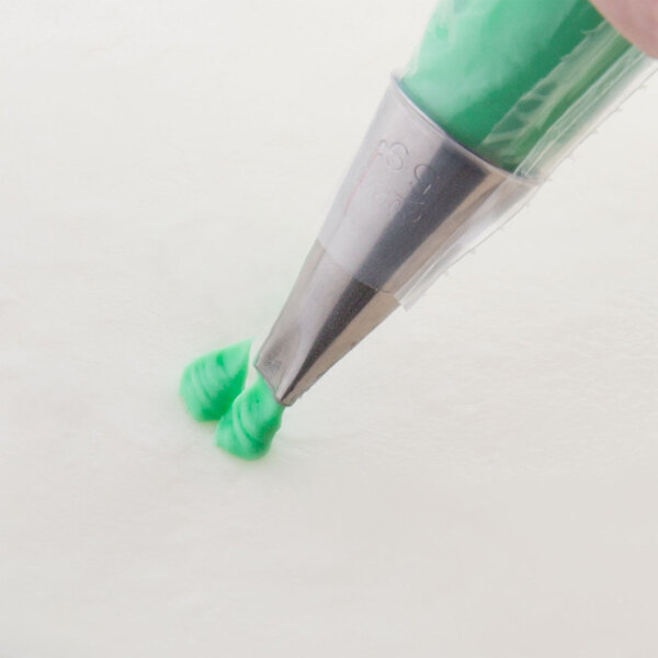 A person using a green Ateco 59A curved petal piping tip to pipe green frosting.