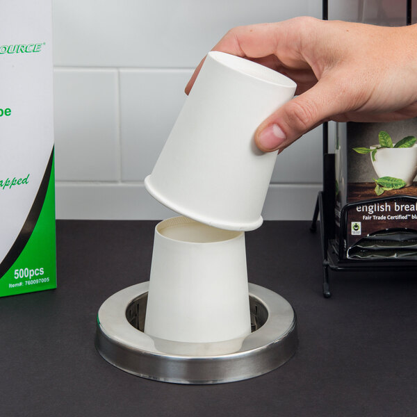 A hand using a San Jamar stainless steel cup dispenser to get a white cup.