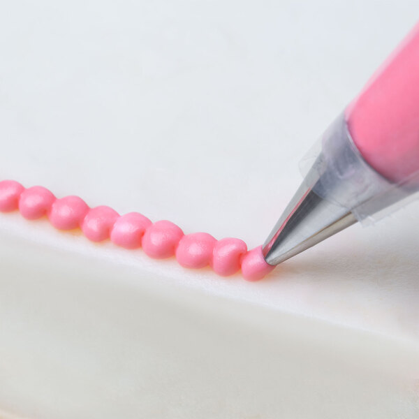 A hand using a pink Ateco oval piping tip to pipe frosting on a cake.