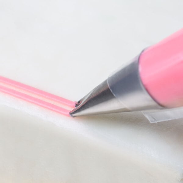A pink Ateco piping tip drawing a line on a cake.