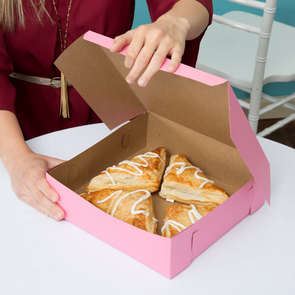 A woman opening a pink pie box with pastries inside.