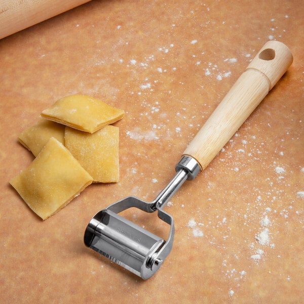 A Fox Run square metal ravioli cutter with a wooden handle next to ravioli.