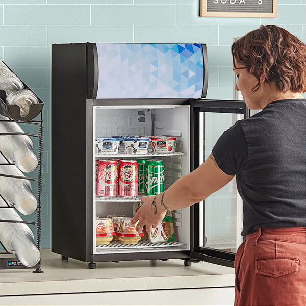 A woman with a black shirt opening the swing door on a black Avantco countertop refrigerator.