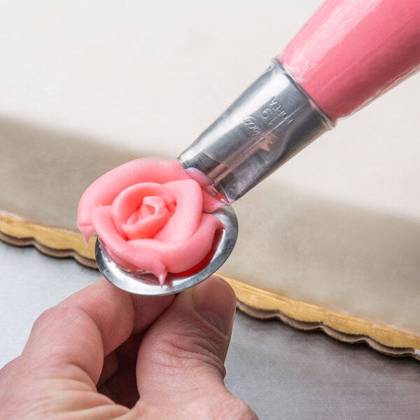 A person using an Ateco rose piping tip to pipe pink frosting on a cake.