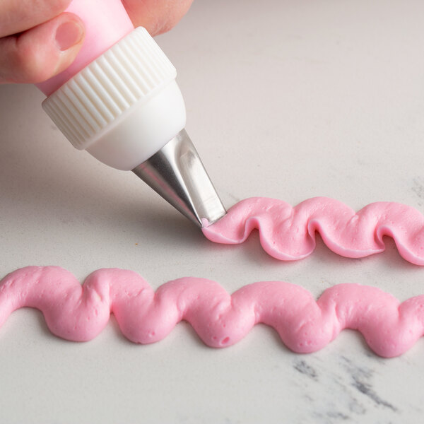 A hand using an Ateco curved petal pastry tip to pipe pink frosting.