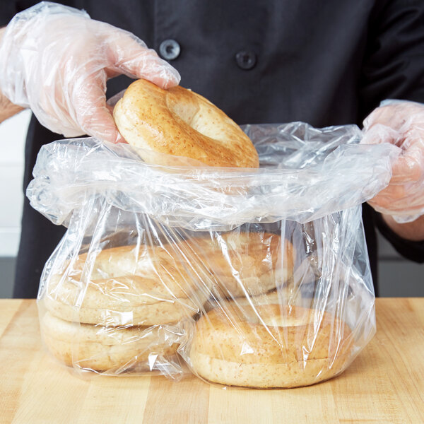 A person holding a bag of bagels in a plastic food bag.