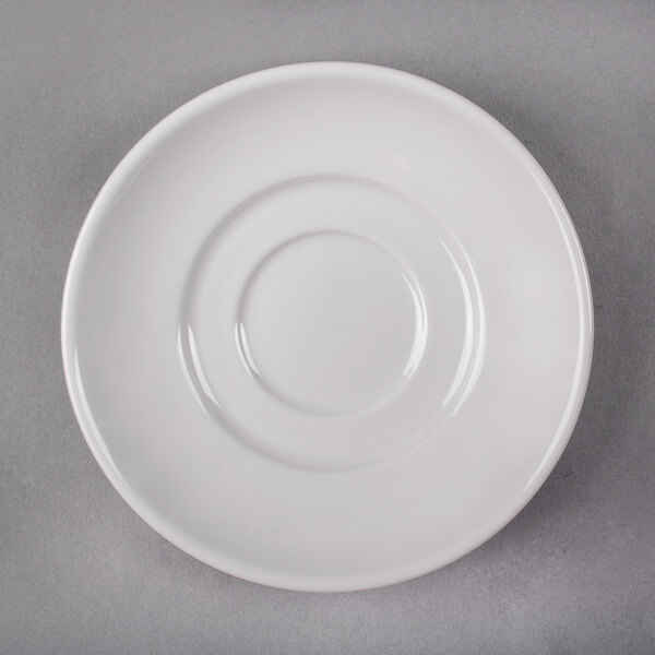 A close-up of a Libbey Rigel Constellation white porcelain saucer with a curved edge and a small hole in the middle.