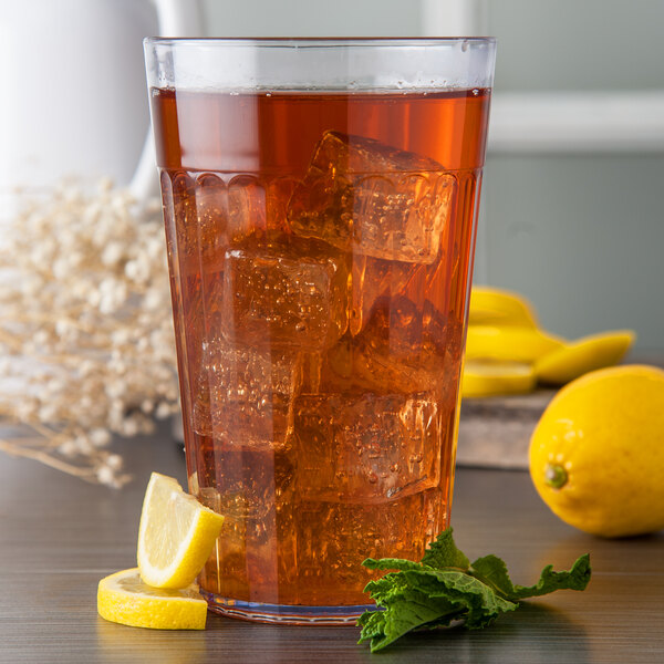 A close up of a Carlisle clear plastic tumbler filled with iced tea, ice, and a lemon wedge.