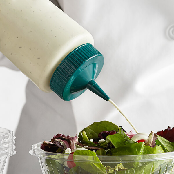 A hand using a Vollrath Traex wide mouth squeeze bottle to pour dressing on a salad.