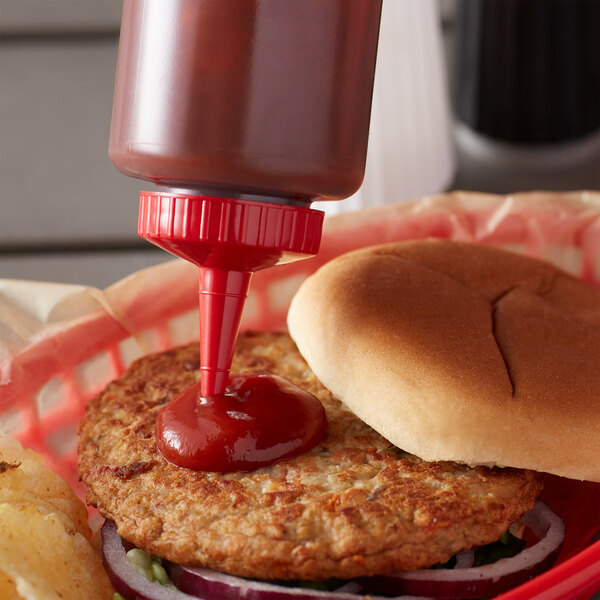 A close-up of a hamburger with a Vollrath Clear Squeeze Bottle of ketchup on a table.