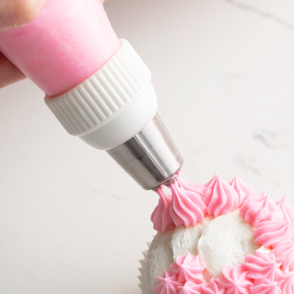 A hand using an Ateco triple star piping tip to pipe pink frosting on a cupcake.