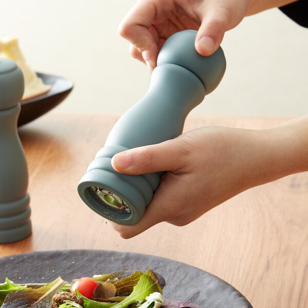 A person using a blue Acopa wooden pepper mill to grind pepper over a plate of food.