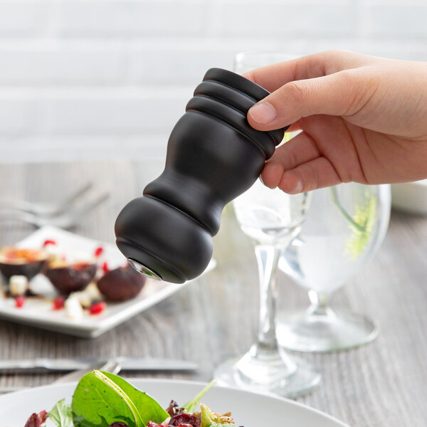 A hand holding a black wooden salt shaker over a salad.