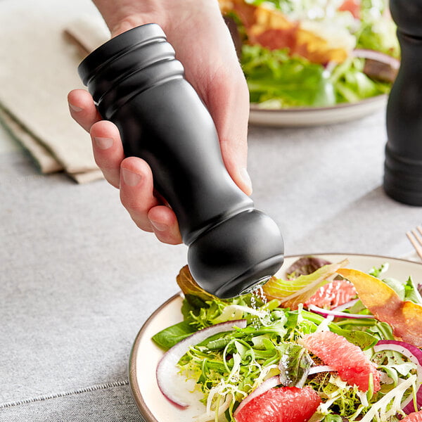 A hand holding a black salt shaker over a salad.