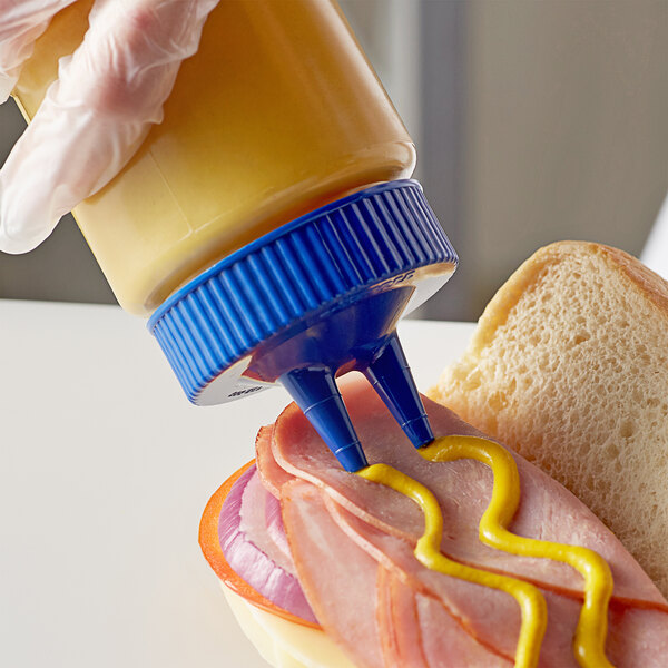 A person pouring mustard from a sandwich into a Vollrath Color-Mate Squeeze Bottle with Blue Cap.