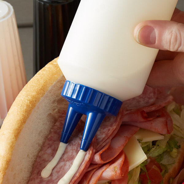 A person pouring mayonnaise into a sandwich using a Vollrath Twin Tip squeeze bottle with a blue cap.