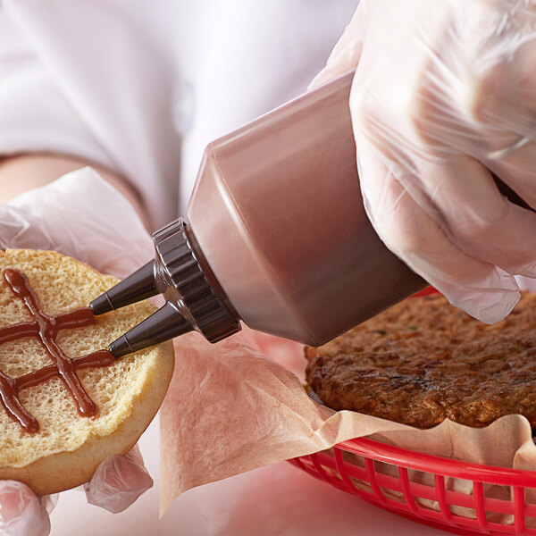 A person pouring sauce from a Vollrath Twin Tip squeeze bottle onto a hot dog bun.