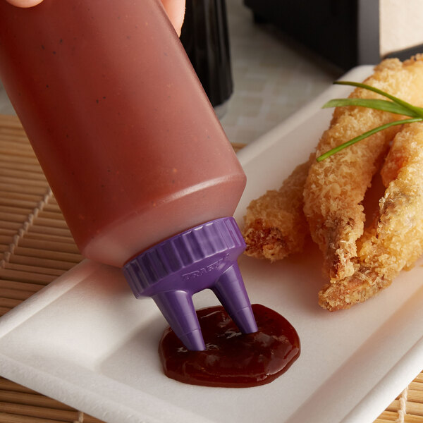 A hand using a Vollrath Twin Tip squeeze bottle with purple cap to pour sauce onto a plate.