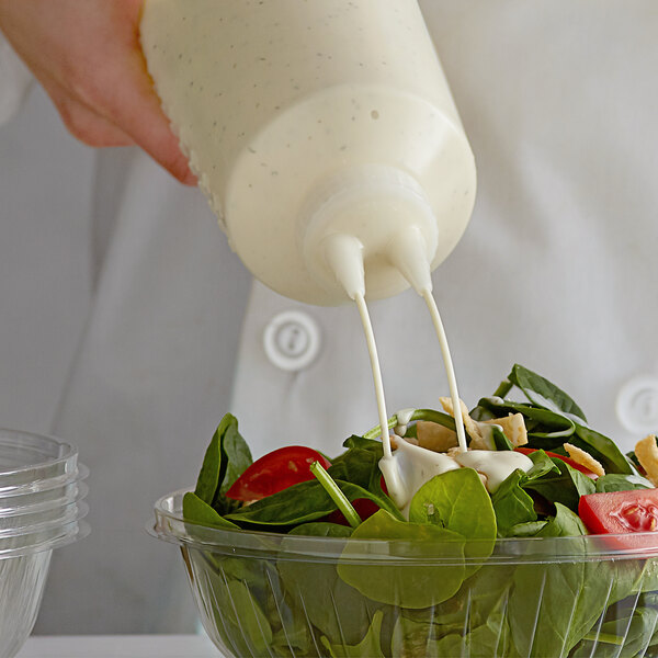 A person using a Vollrath Twin Tip Squeeze Bottle to pour white dressing onto a spinach salad.