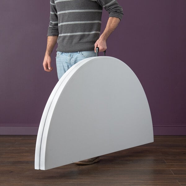 A person holding a Lancaster Table & Seating white plastic bi-folding table with a white granite finish.