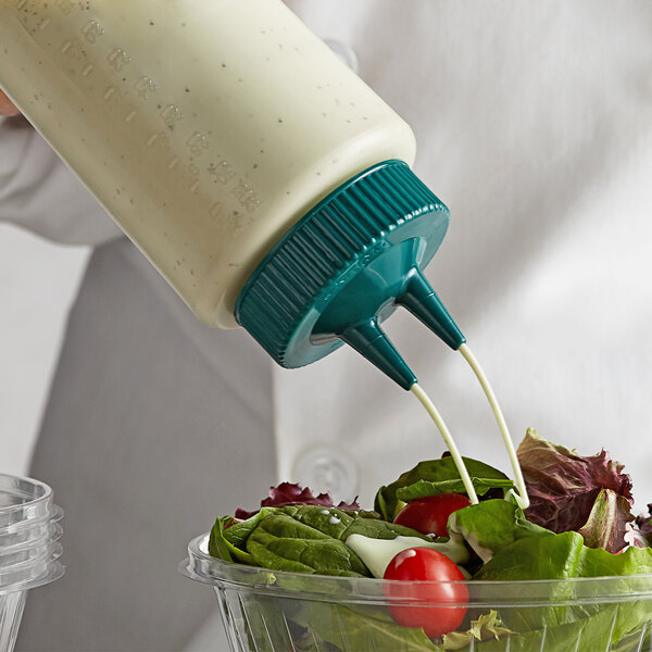 A person using a Vollrath Color-Mate squeeze bottle to pour dressing onto a salad.