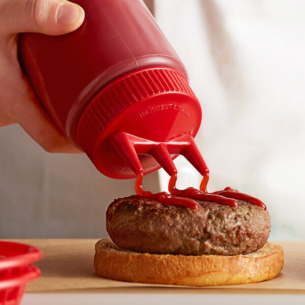 A person using a Vollrath Tri Tip squeeze bottle to pour ketchup on a burger.