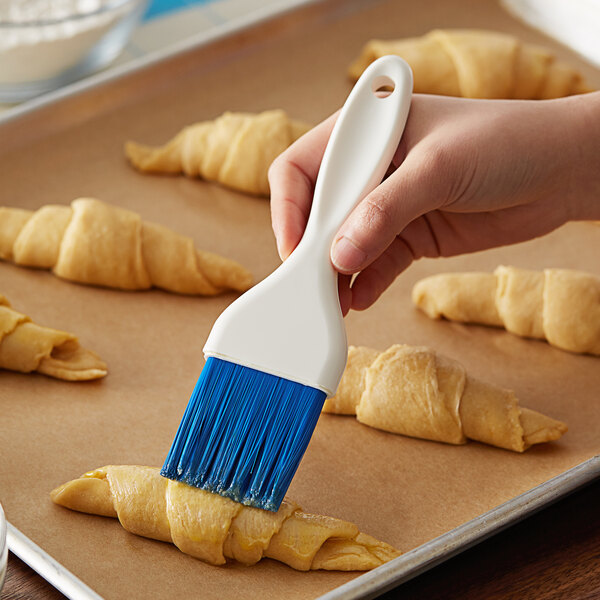 A person using a Carlisle Sparta Spectrum pastry brush to baste croissants.
