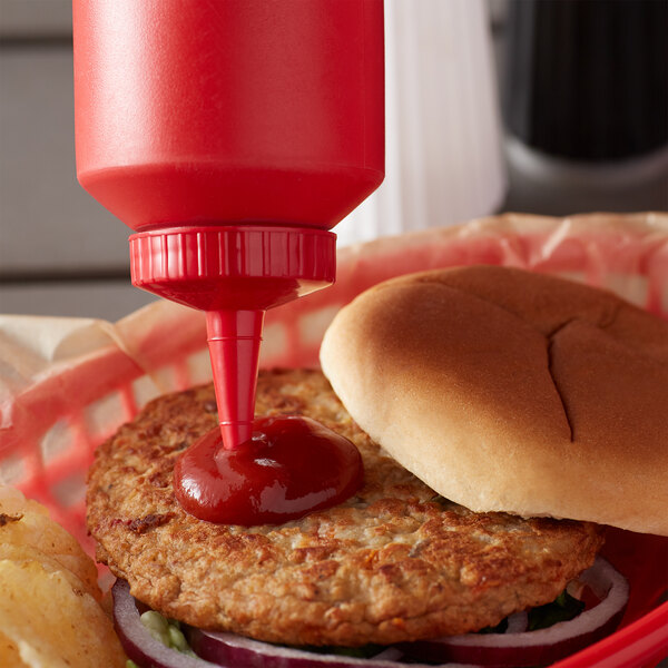 A hamburger with ketchup on a plate with fries and a squeeze bottle of ketchup.