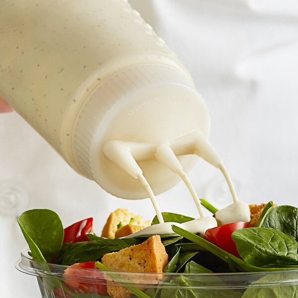 A person pouring dressing from a Vollrath Tri Tip Squeeze Bottle onto a salad.