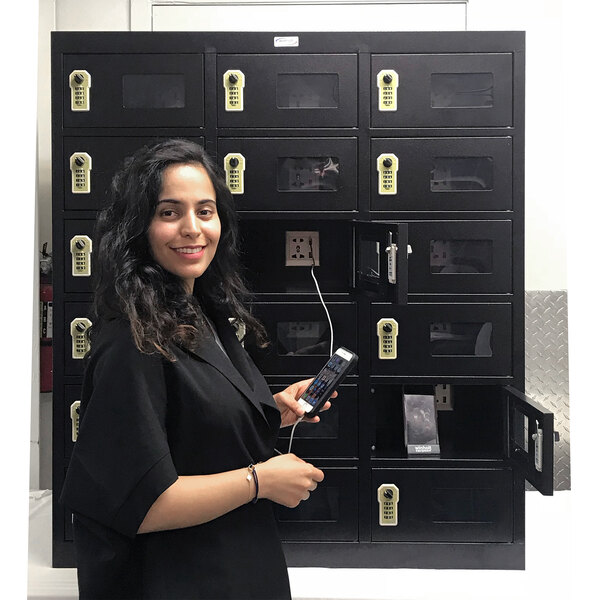 A woman holding a phone in front of a Winholt smart locker with perforated doors.