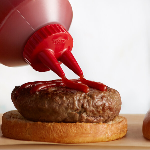 A ketchup bottle with a Vollrath red bottle cap being poured onto a burger.