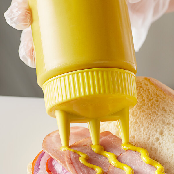 A person using a Vollrath yellow Tri Tip squeeze bottle to pour mustard on a sandwich.