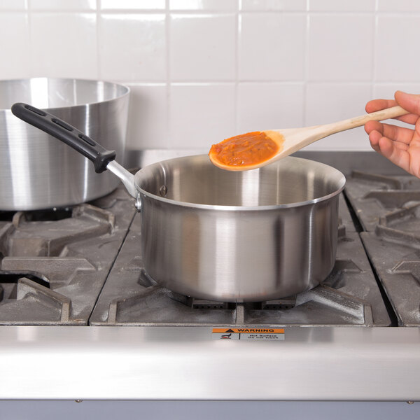 A person stirring red sauce in a Vollrath stainless steel sauce pan on a stove.