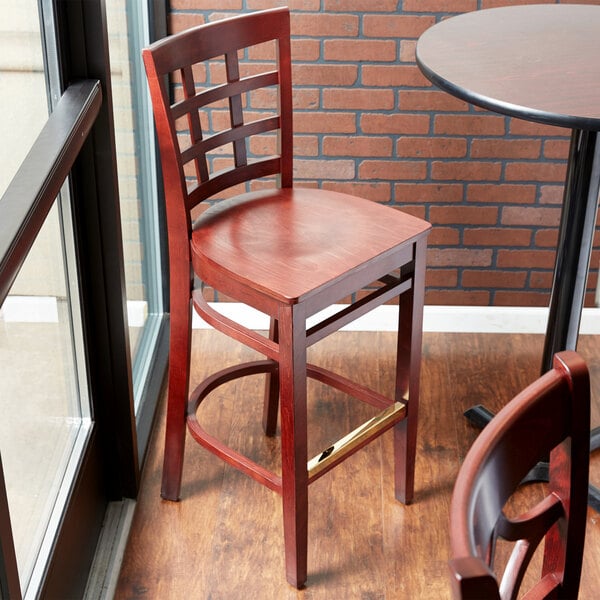 A Lancaster Table & Seating mahogany wood bar stool seat on a table in a restaurant.