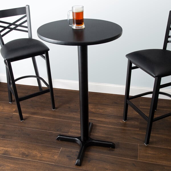 A Lancaster Table & Seating black metal bar table with a reversible cherry/black top and cross base plate with two black chairs.