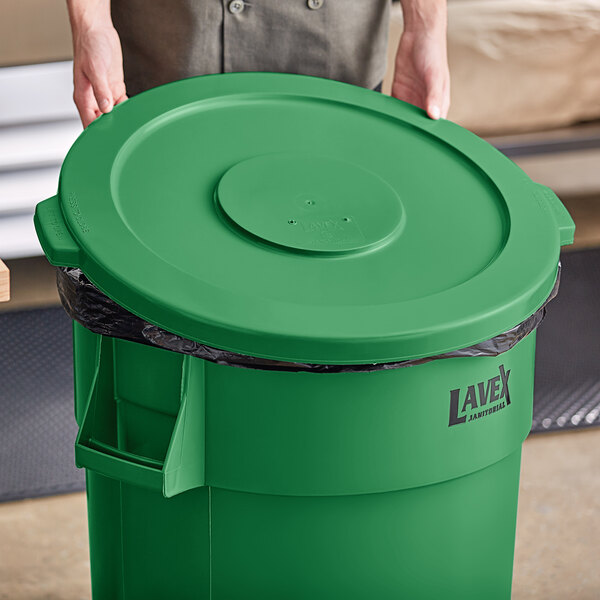 A person holding a Lavex green commercial trash can lid.