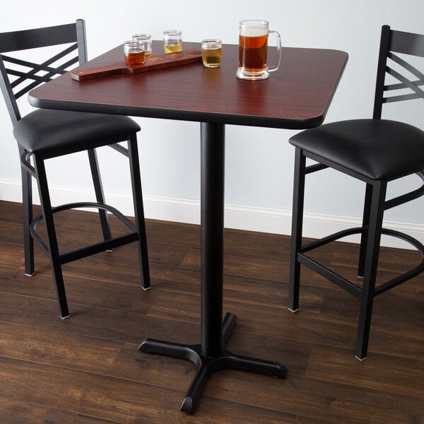 A Lancaster Table & Seating bar table with glasses of beer on it and two chairs.