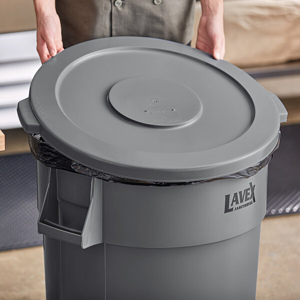A person holding a gray Lavex round commercial trash can lid.