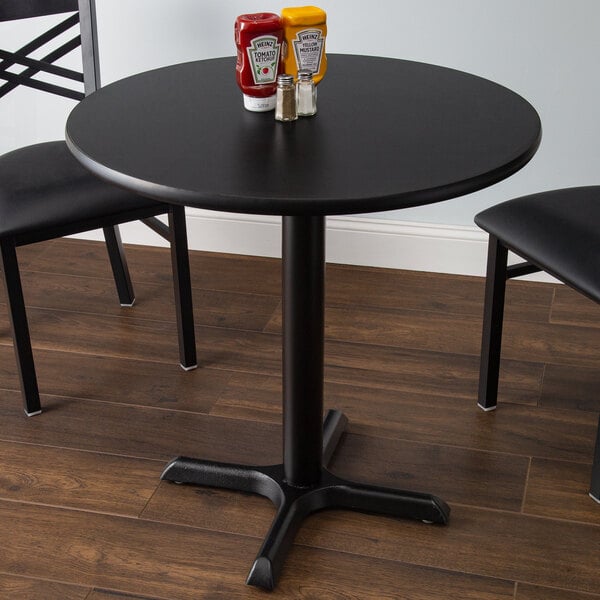 A black table with a Lancaster Table and Seating black table top and cross cast iron base plate on a table in a restaurant dining area.