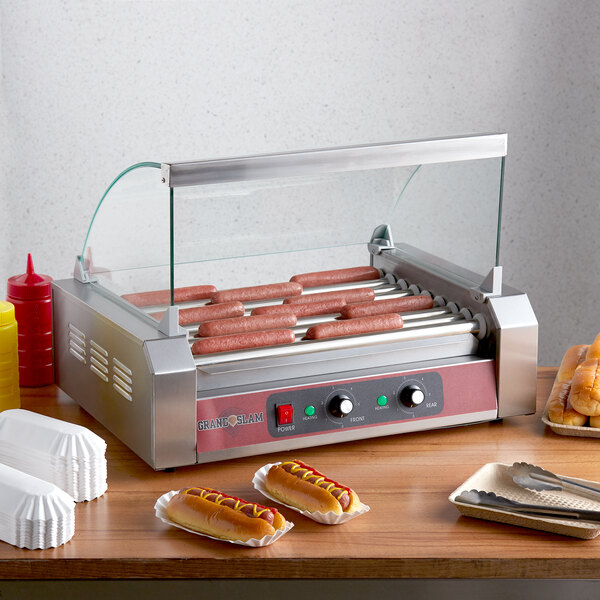 A Grand Slam hot dog roller grill on a counter with hot dogs and condiments.