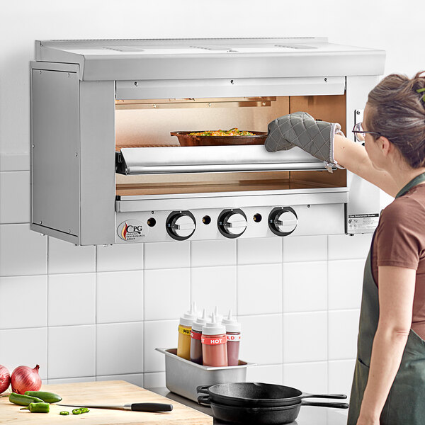 A woman in an apron using a Cooking Performance Group infrared salamander broiler.