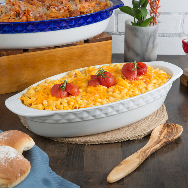A white Tuxton oval casserole dish with macaroni and cheese on a table.