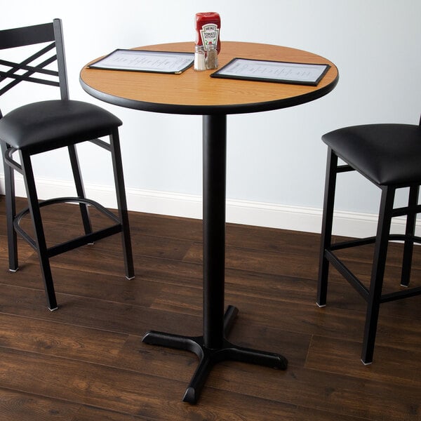 A Lancaster Table & Seating bar height table with a round reversible walnut and oak table top on a cross cast iron base with chairs.