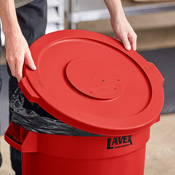 A person opening a red Lavex round commercial trash can lid.